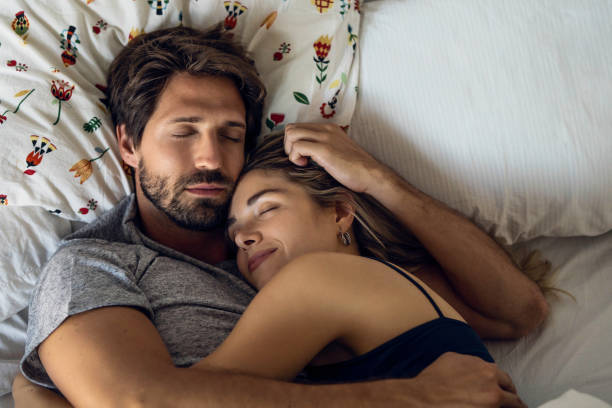 Overhead view of young couple hugging while sleeping on bed in bedroom